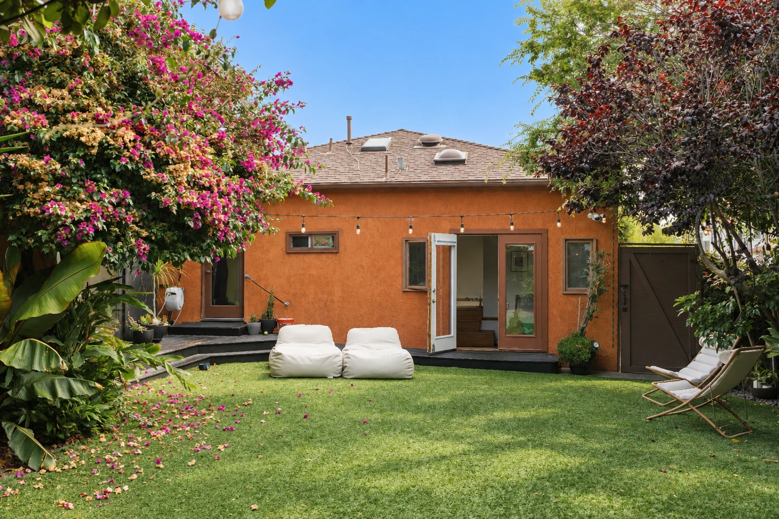 Main house across the green courtyard with open French doors, bougainvillea, and garden seating